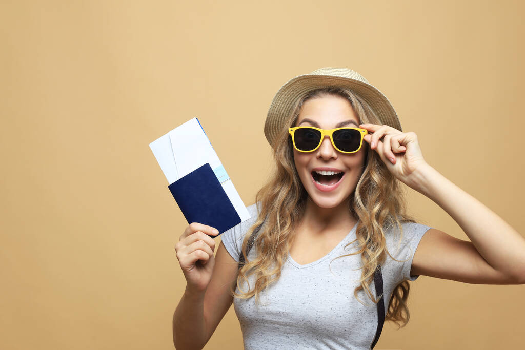 Gyönyörű szőke nő napszemüvegben pózol útlevéllel jegyek felett bézs háttér - Fotó, kép