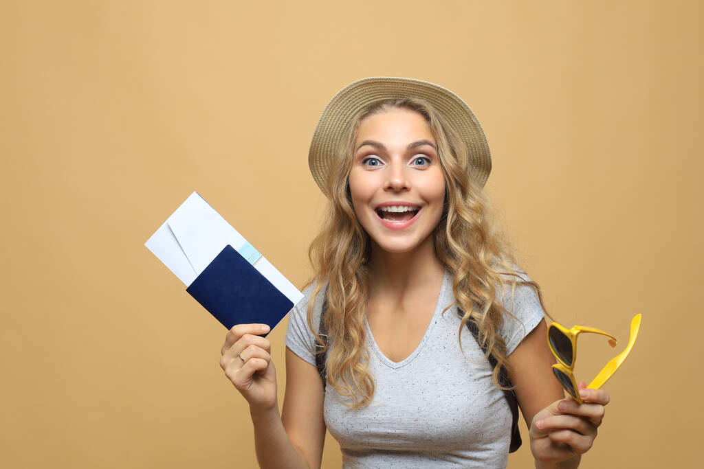 Gyönyörű szőke nő napszemüveg pózol útlevéllel jegyek felett bézs háttér - Fotó, kép
