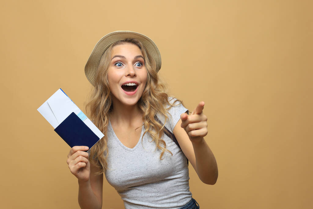 Красивая блондинка в летней одежде позирует с паспортом с билетами на бежевый фон
 - Фото, изображение