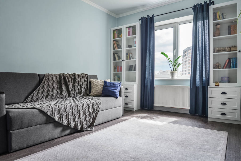 Leichtes gemütliches Teenzimmer mit weißen Bücherregalen, grauem Sofa und blauer Wand - Foto, Bild