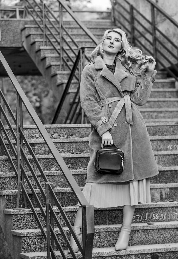 Dívka teplý kabát stojí městské schody pozadí. Vytvořit podzimní oblečení cítit pohodlně a pěkně. Podzimní oblečení. Žena nosí stylové oblečení a kabelku. Outerwear z moderní teplé a stylové ekologické kožešiny - Fotografie, Obrázek