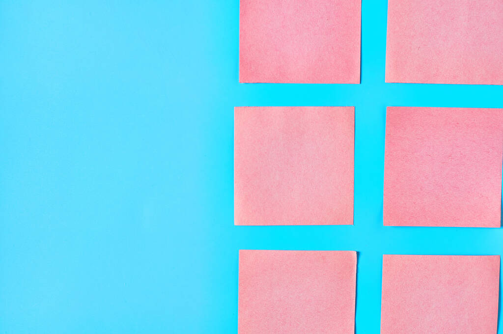 Рядки рожевих квадратних порожніх паперових наклейок на синьому фоні. Копіювати простір. Вид зверху
 - Фото, зображення