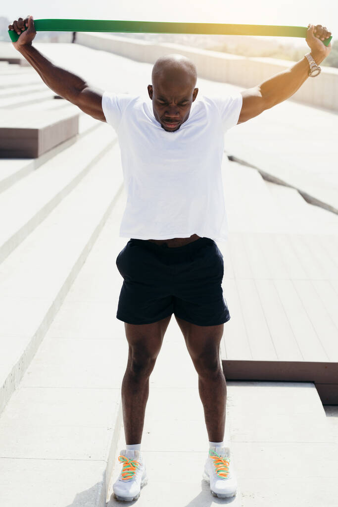 O atleta negro profissional da África está envolvido em esportes ao ar livre. Estique fita elástica sobre a cabeça para fortalecer as mãos
. - Foto, Imagem
