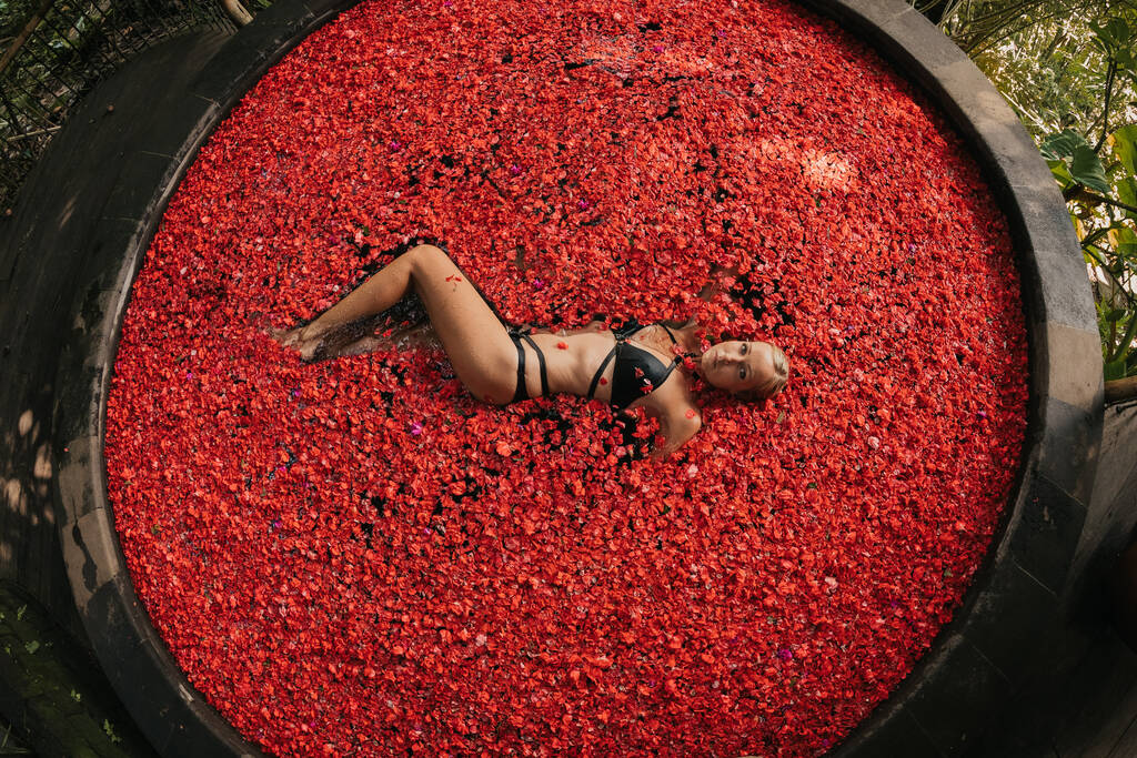 junges blondes Mädchen im Pool mit roten Rosenblättern - Foto, Bild