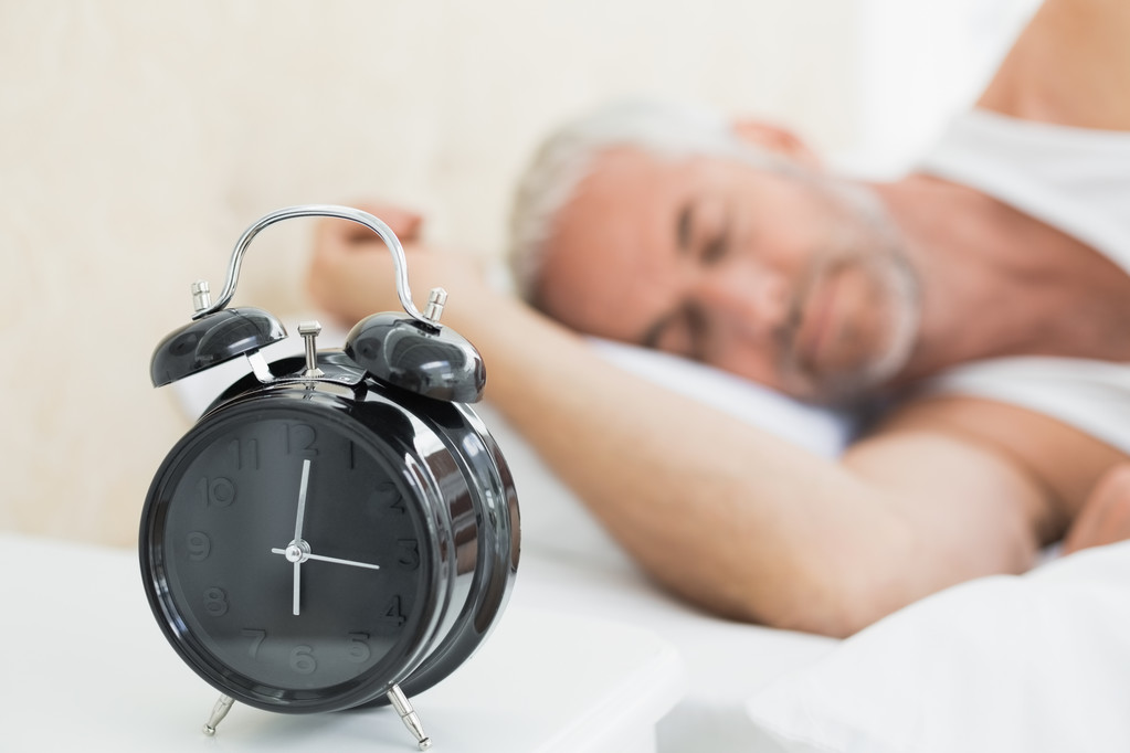 Homem dormindo na cama com despertador em primeiro plano
 - Foto, Imagem