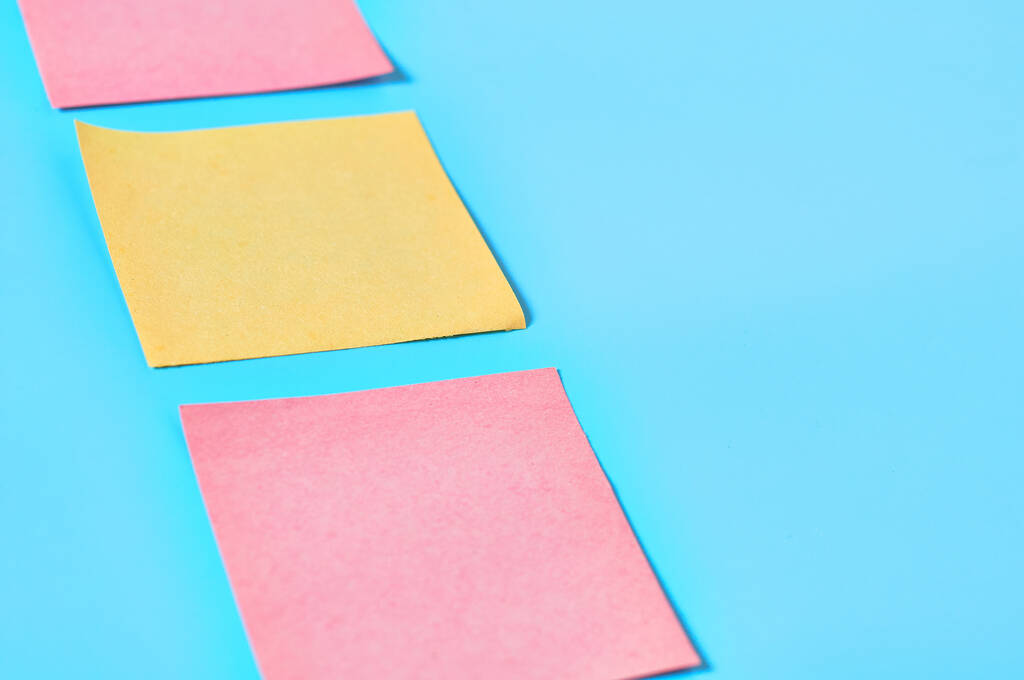 Fila de pegatinas de papel en blanco cuadradas amarillas y rojas sobre fondo azul. Copiar espacio
 - Foto, imagen