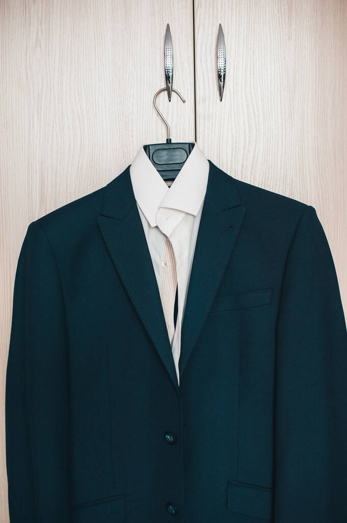 Part of stylish menswear. White shirt and blue black jacket on the rack. Against the background of bright cabinets. Morning groom. wedding day. Close, close up. classic style. place for text on hanger - Photo, Image