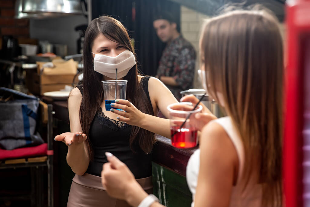 les filles en masques médicaux bavardant dans un pub. Les filles avec des masques médicaux parlent au bar. filles dans les masques médicaux boire des cocktails
 - Photo, image