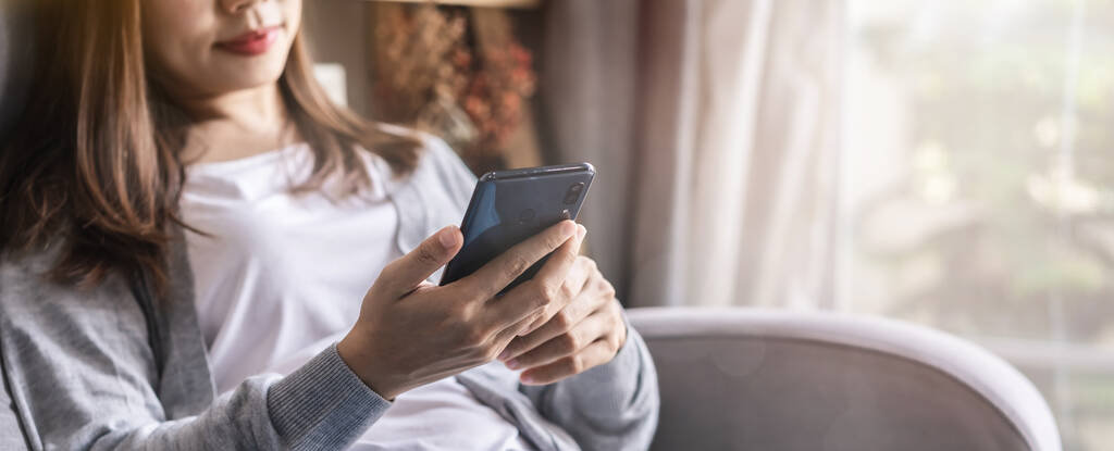 Jeune femme allongée sur un canapé dans le salon et utilisant un téléphone portable à la maison, bannière Web avec espace de copie
 - Photo, image