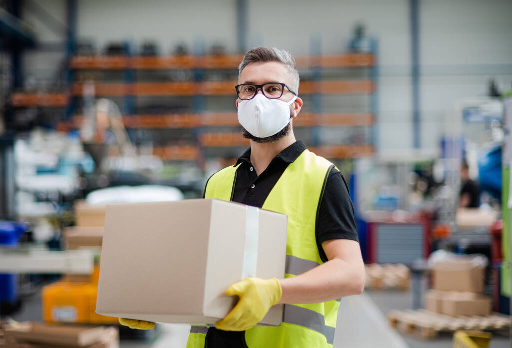 工業工場や倉庫で働く保護マスクを持つ男労働者. - 写真・画像