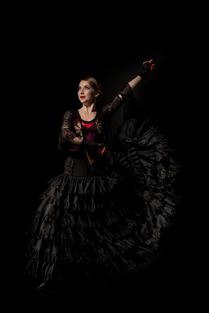 Χαρούμενος χορευτής φλαμένκο ντυμένος κρατώντας καστανέτες και χορεύοντας απομονωμένος στα μαύρα - Φωτογραφία, εικόνα