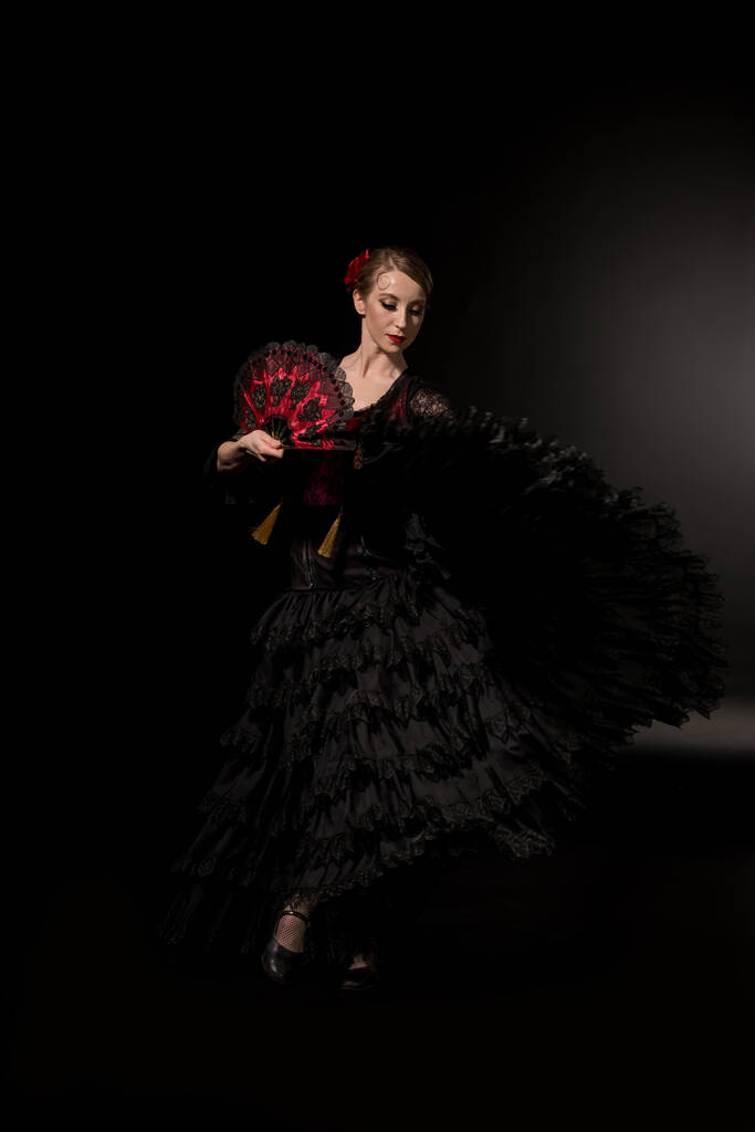 joven bailarina de flamenco sosteniendo abanico y bailando sobre negro
  - Foto, Imagen