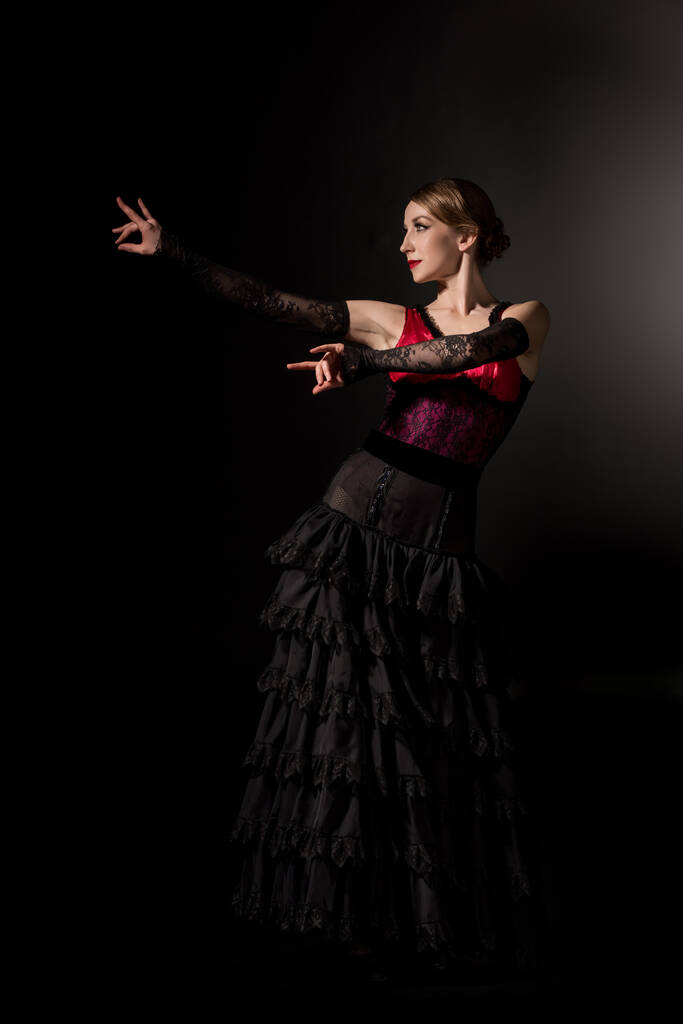 elegante mujer haciendo gestos y bailando flamenco sobre negro
  - Foto, Imagen