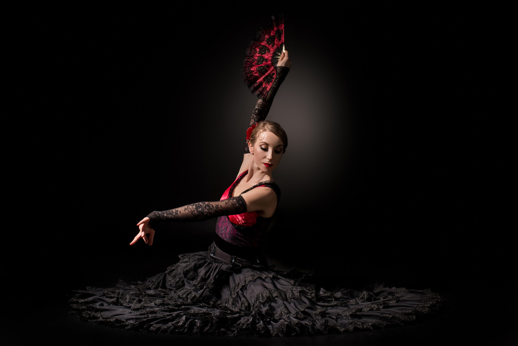 молодая танцовщица фламенко держит веер, сидя на черном
 - Фото, изображение