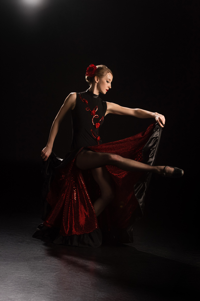 side view of young woman touching dress and dancing flamenco on black  - Photo, Image