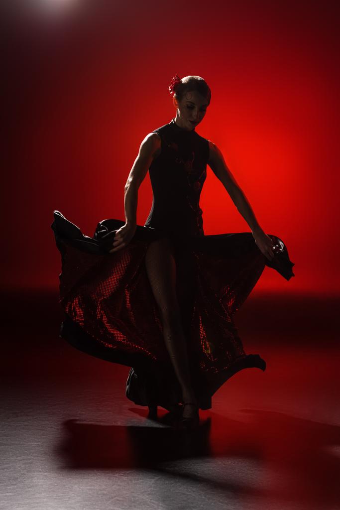 Силуэт молодой женщины, касающейся платья и танцующего фламенко на красном
 - Фото, изображение