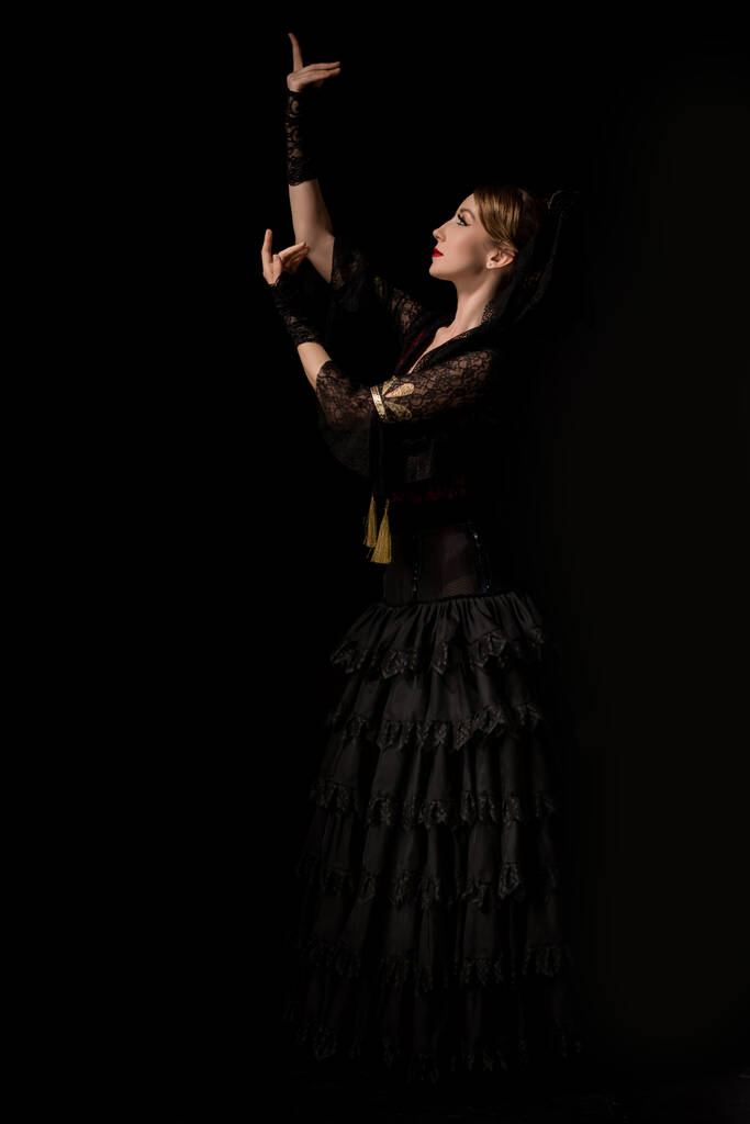 πλαϊνή όψη όμορφης χορεύτριας φλαμένκο που χορεύει απομονωμένη σε μαύρο  - Φωτογραφία, εικόνα