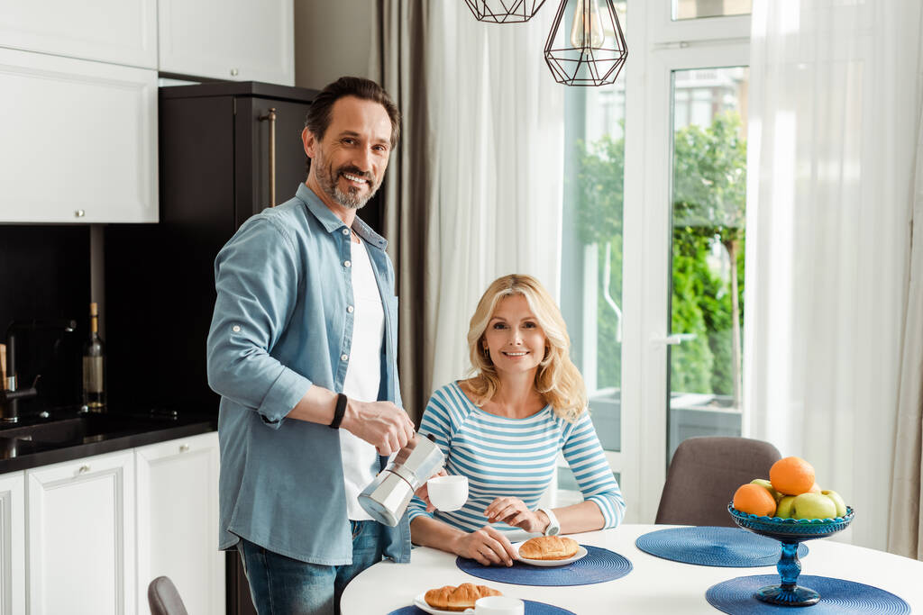 Зріла пара посміхається на камеру під час сніданку на кухні
  - Фото, зображення