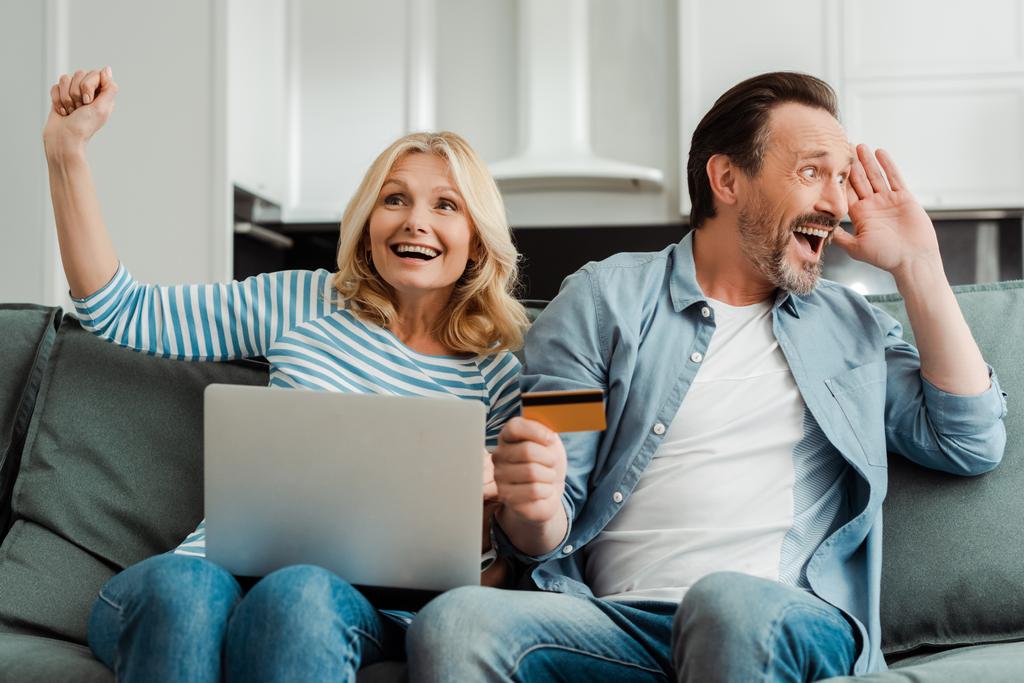 Couple mature excité avec ordinateur portable et carte de crédit sur le canapé à la maison
  - Photo, image