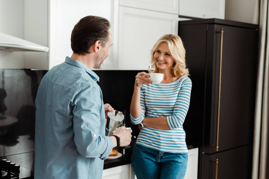 Kaunis nainen hymyilee aviomies kaatamalla kahvia keittiössä  - Valokuva, kuva