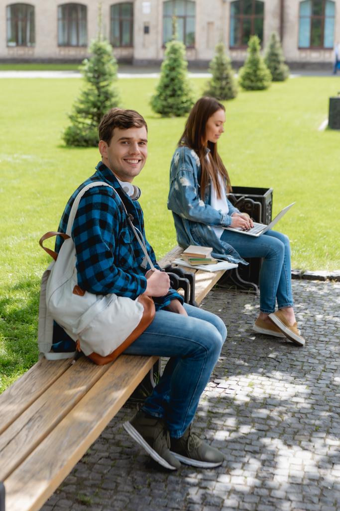 selektywne skupienie szczęśliwy student uśmiecha się podczas gdy dziewczyna za pomocą laptopa w pobliżu kampusu uniwersyteckiego, koncepcja studiów online  - Zdjęcie, obraz