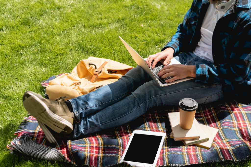 vue recadrée de l'étudiant à l'aide d'un ordinateur portable près de la tablette numérique avec écran blanc et tasse en papier sur couverture à carreaux, concept d'étude en ligne
  - Photo, image