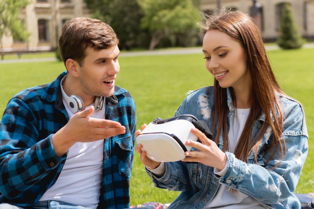 schöner Mann zeigt mit der Hand auf Virtual-Reality-Headset neben fröhlichem Mädchen  - Foto, Bild