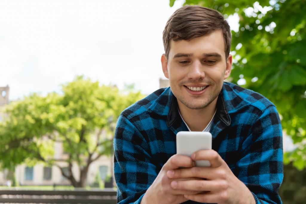 estudiante guapo sonriendo mientras usa el teléfono inteligente
  - Foto, Imagen