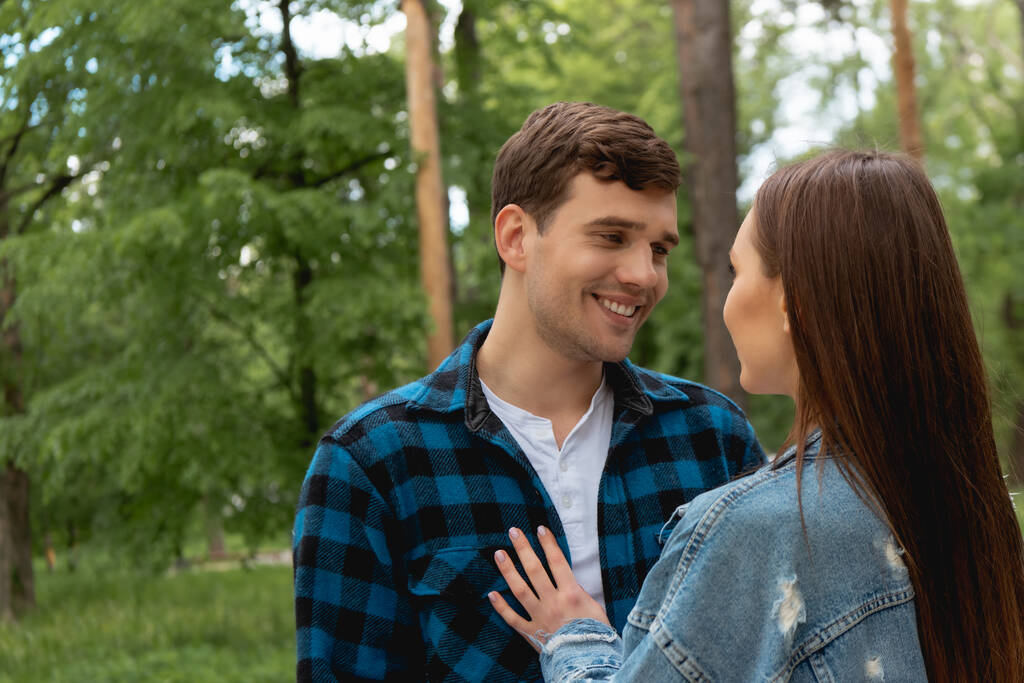 cheerful student looking at girlfriend in denim jacket in park  - Photo, Image