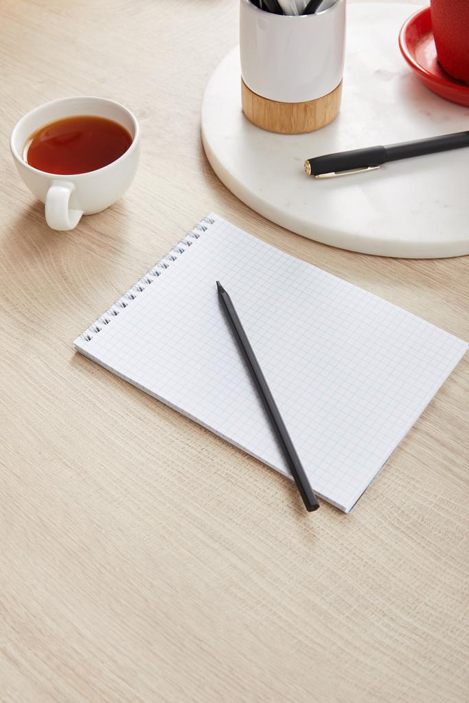 kopje thee en blanco notitieboekje met potlood en pen op houten ondergrond - Foto, afbeelding