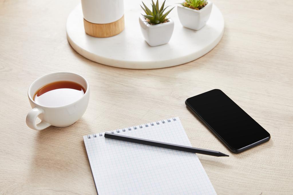 plantas verdes, taza de té y cuaderno en blanco con lápiz cerca de teléfono inteligente en la superficie de madera
 - Foto, imagen