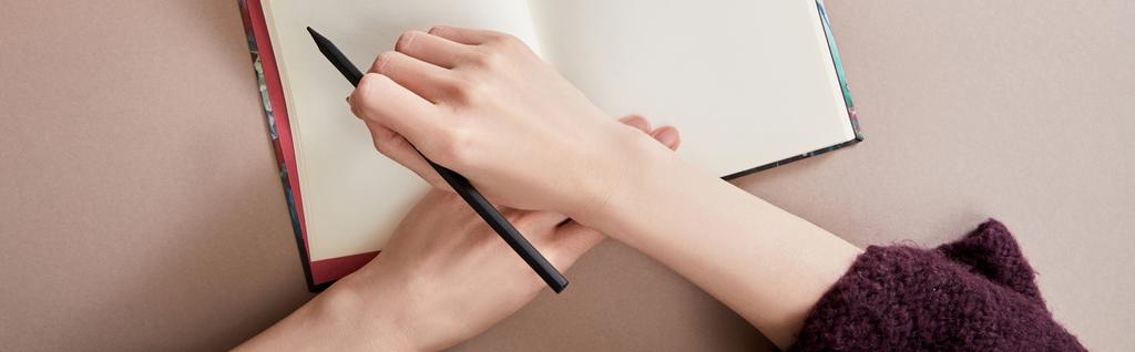 vista recortada de la mujer escribiendo en cuaderno en la superficie beige, plano panorámico
 - Foto, imagen