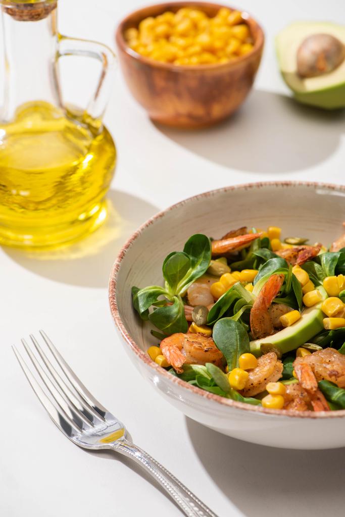вид на свежий зеленый салат с креветками и авокадо на тарелке возле столовых приборов на белом фоне
 - Фото, изображение