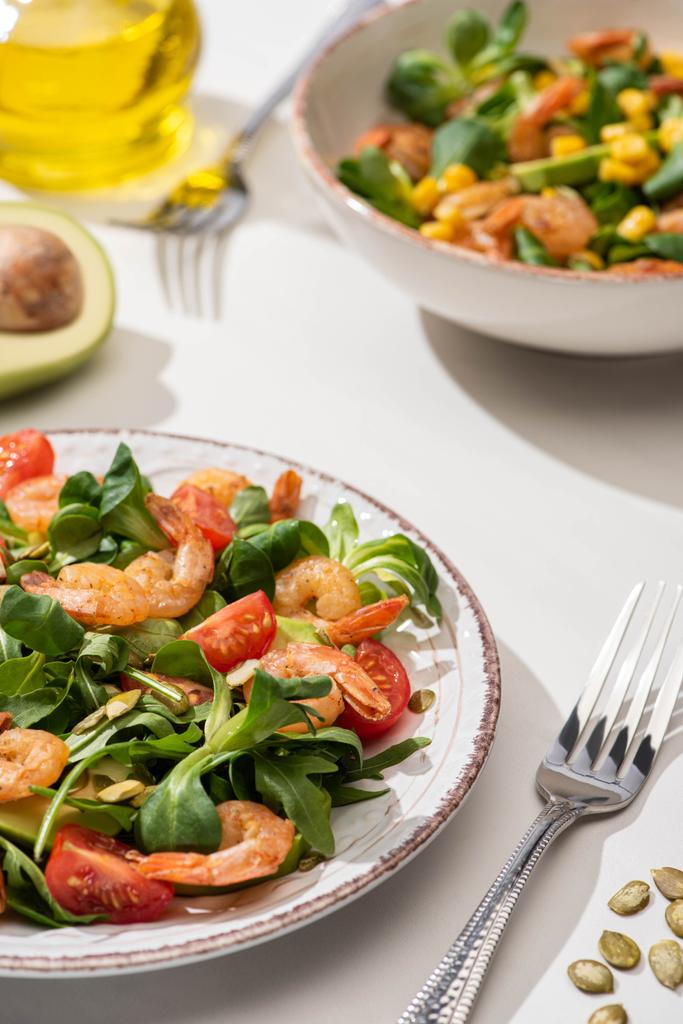 selective focus of fresh green salad with shrimps and avocado on plates near forks on white background - Photo, Image