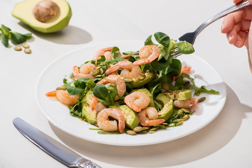 partial view of woman eating fresh green salad with pumpkin seeds, shrimps and avocado on white background - Photo, Image