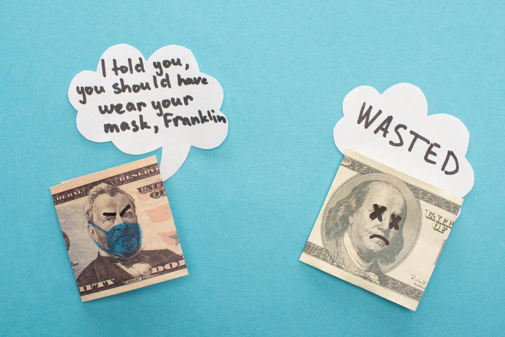 bovenaanzicht van dollarbankbiljetten met getekend medisch masker en spraakbellen op blauwe achtergrond - Foto, afbeelding