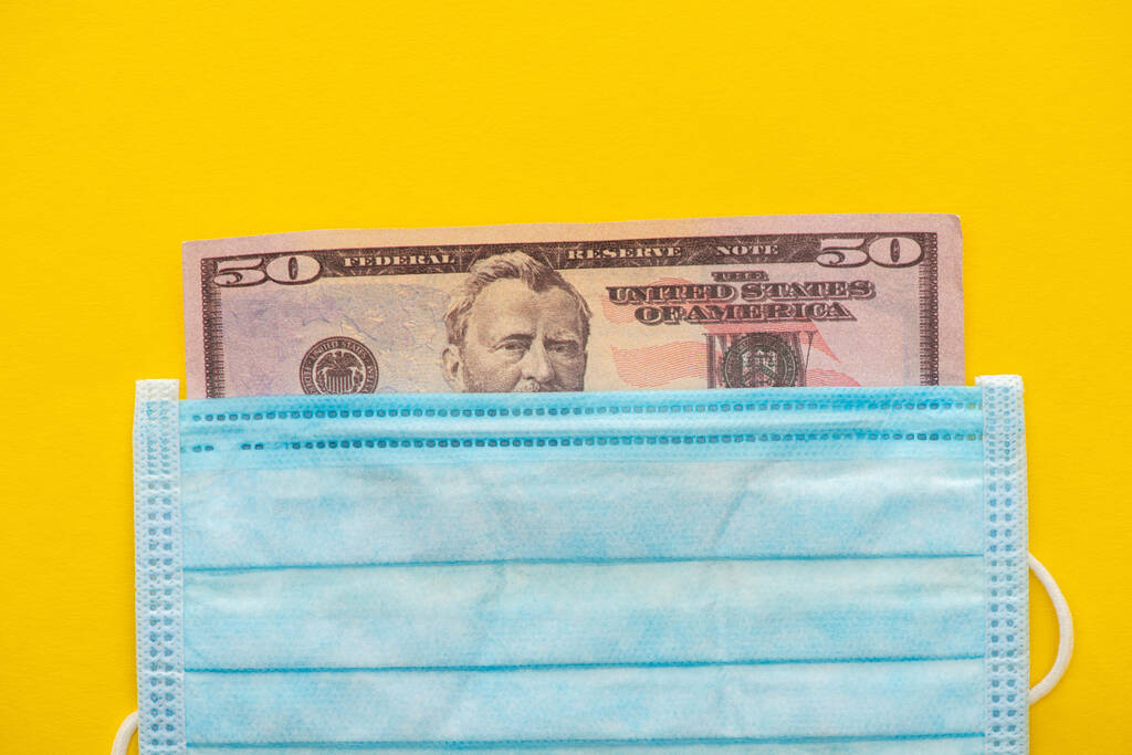 Draufsicht auf Dollar-Banknote und medizinische Maske auf gelbem Hintergrund - Foto, Bild