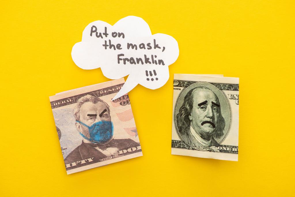 黄色の背景に音声バブルの近くに医療用マスクと顔の表情が描かれた銀行券のトップビュー - 写真・画像