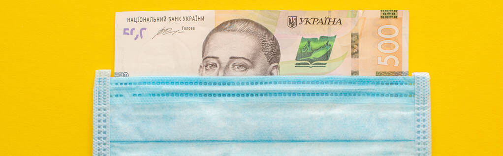 vista superior da nota ucraniana e máscara médica sobre fundo amarelo, tiro panorâmico
 - Foto, Imagem