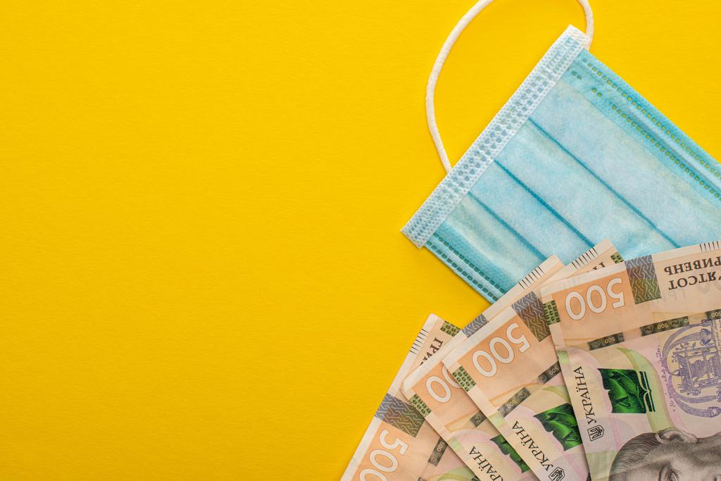 Sarı arka planda Ukrayna banknotlarının ve tıbbi maskenin üst görüntüsü - Fotoğraf, Görsel