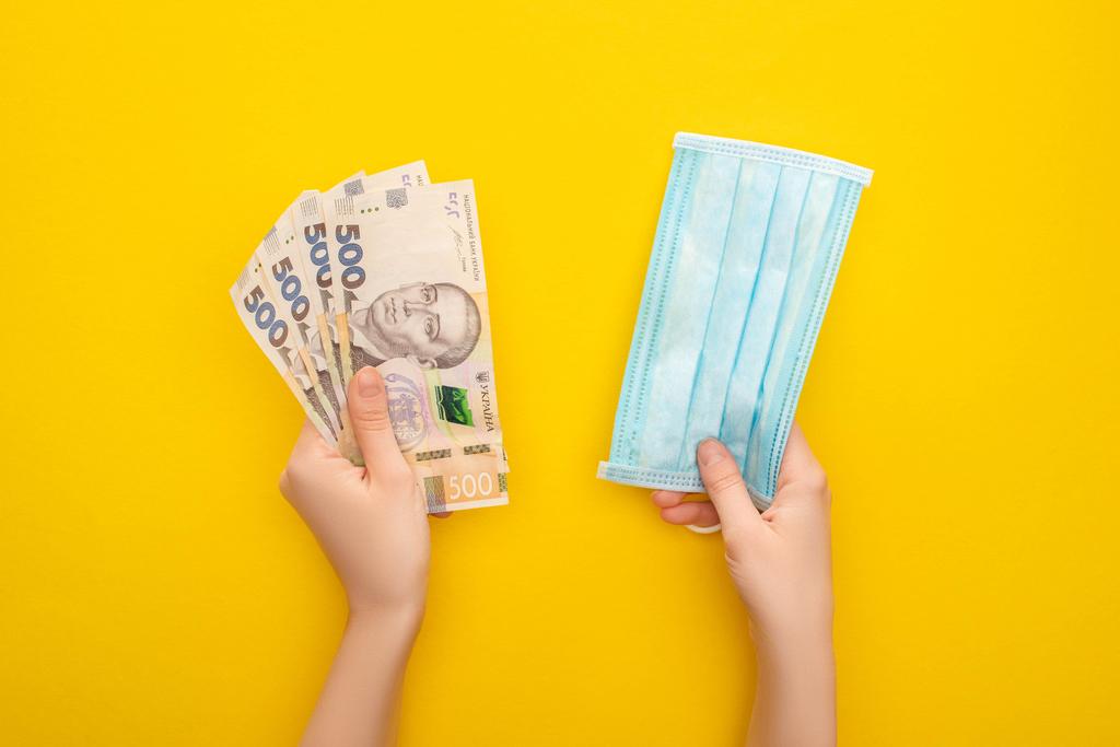 Частковий погляд на жінку, що тримає українські банкноти та медичну маску на жовтому тлі. - Фото, зображення
