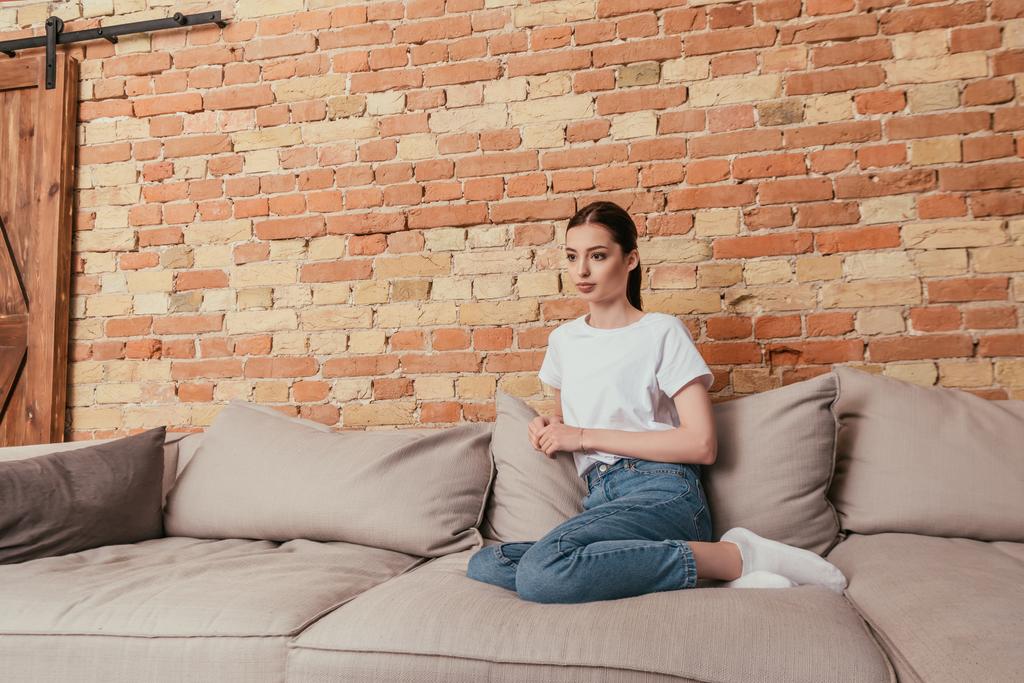 atrakcyjna młoda kobieta siedzi na sofie z miękkimi poduszkami - Zdjęcie, obraz