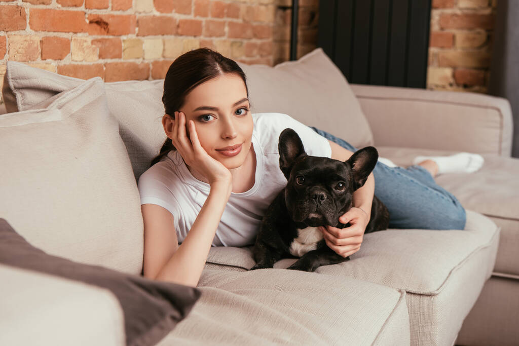 selectieve focus van jonge vrouw liggend op de bank met zwart frans bulldog  - Foto, afbeelding