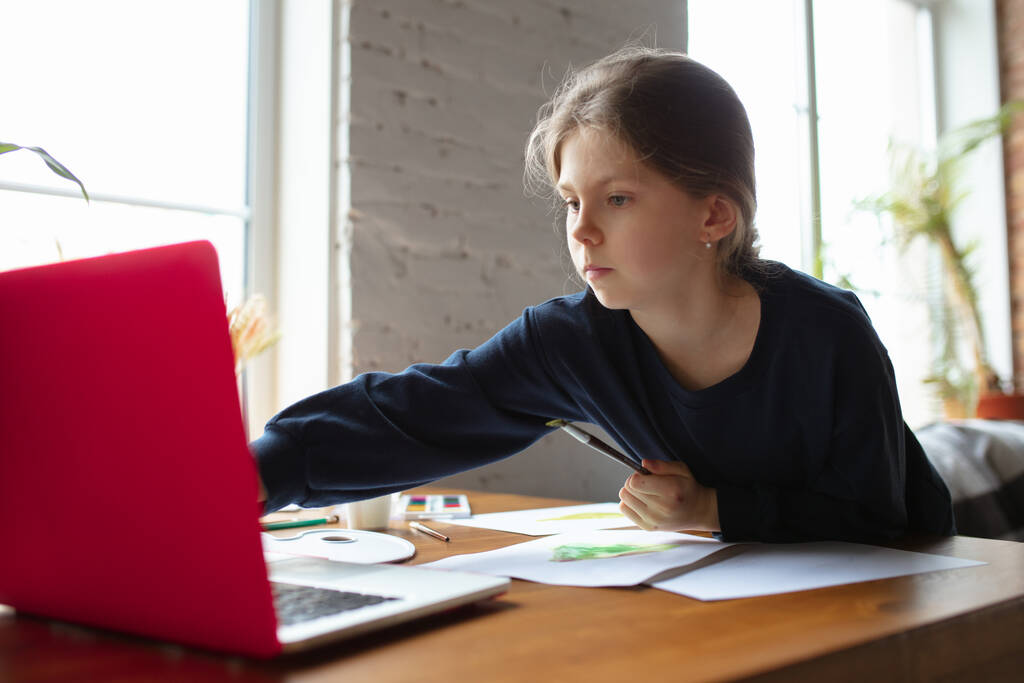 Meisje tekening met verf en potloden thuis, kijken naar docenten tutorial op laptop. Digitalisering, onderwijs op afstand - Foto, afbeelding