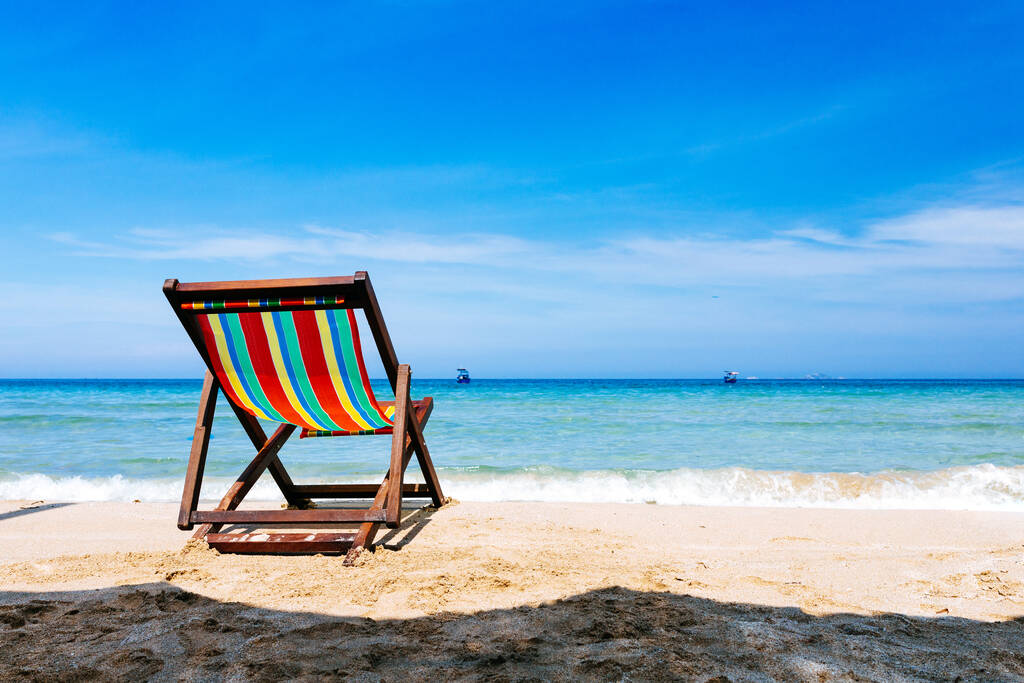 Cadeira de convés na praia junto ao mar. A cor negra da água e o céu azul com nuvens quebradas no fundo. Um lugar para relaxamento e trabalho freelance. Vista mar aberto com barcos no horizonte
 - Foto, Imagem