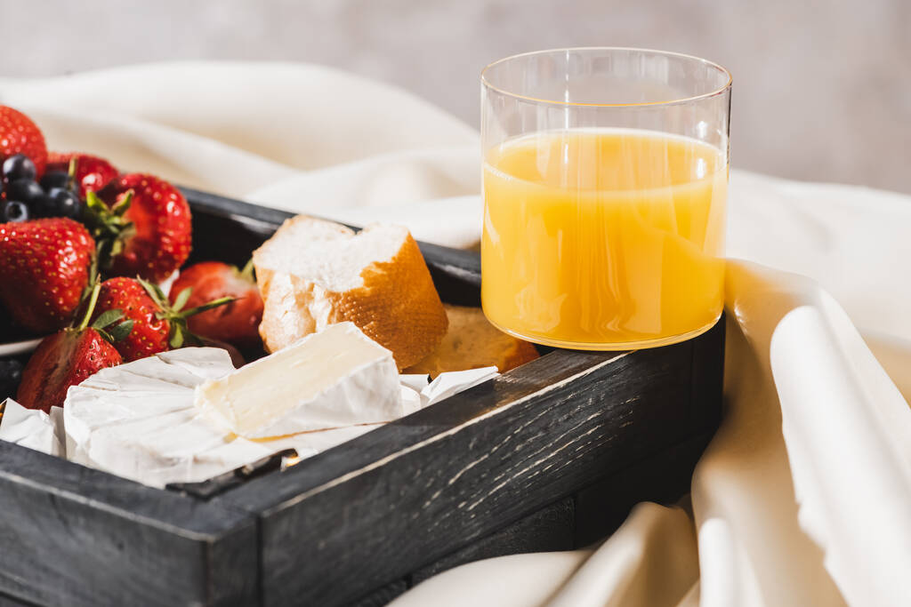 Nahaufnahme des französischen Frühstücks mit Camembert, Orangensaft, Beeren und Baguette auf Holztablett auf texturiertem weißen Tuch - Foto, Bild
