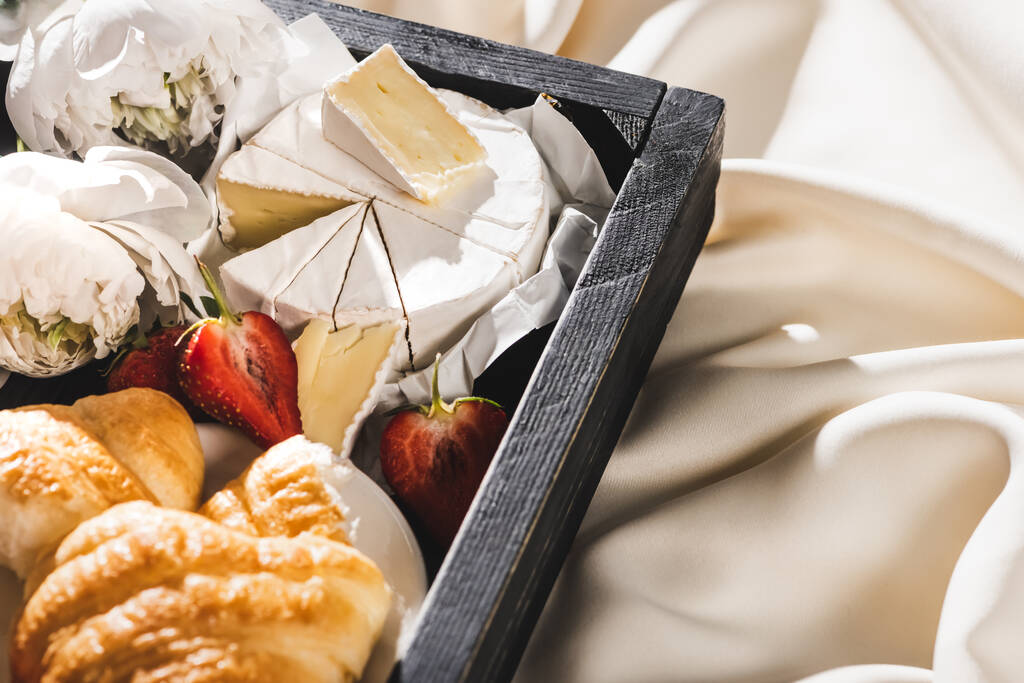 закрытый вид на французский завтрак с круассаном, камембером, клубникой на деревянной дорожке на текстурированной белой ткани с пионами
 - Фото, изображение