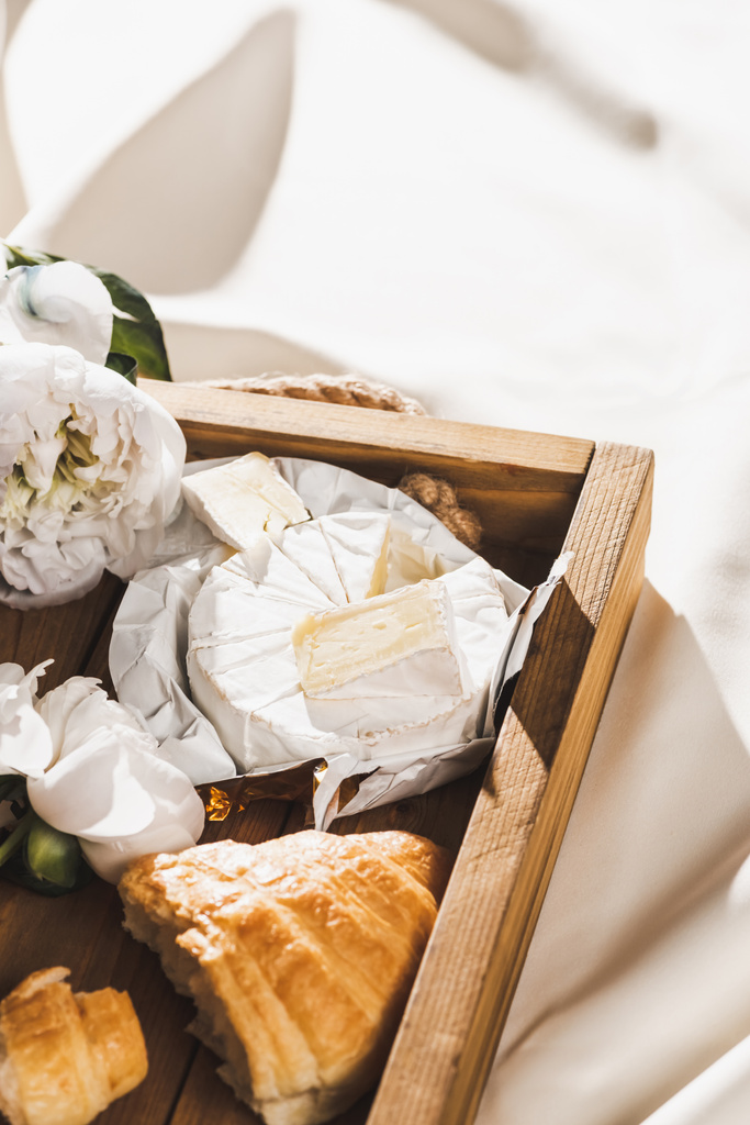 vue rapprochée du petit déjeuner français avec croissant, Camembert sur plateau en bois sur toile blanche texturée avec pivoine
 - Photo, image
