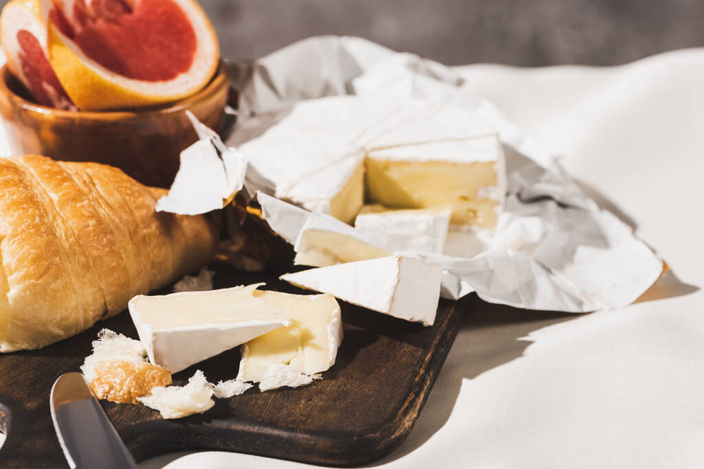 enfoque selectivo de desayuno francés con croissant, Camembert, pomelo sobre tabla de cortar de madera en mantel blanco
 - Foto, Imagen