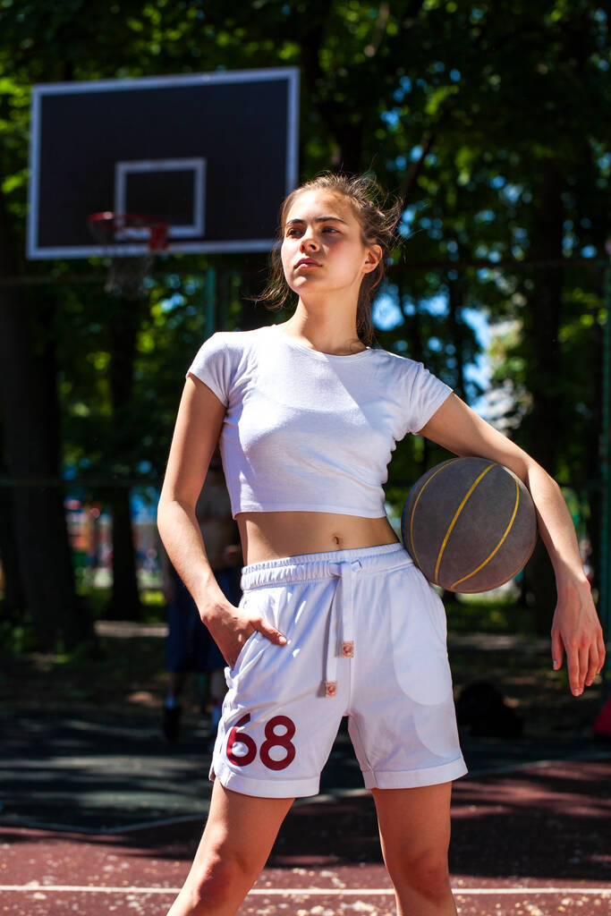 Fiatal gyönyörű lány egy kosárlabda pózol a játszótéren - Fotó, kép